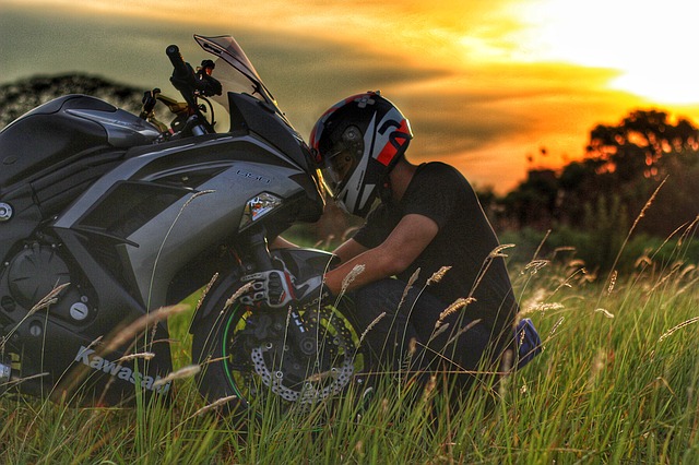 Človek s moto-prilbou opravuje svoju motorku na lúke, Kawasaki